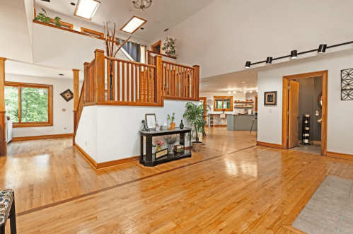 Spacious interior with wooden floors, a staircase, and natural light from large windows, leading to a kitchen area.