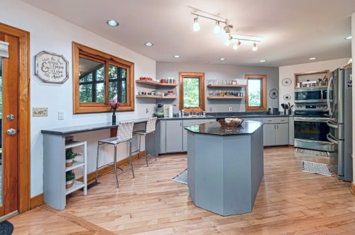 Modern kitchen with gray cabinets, an island, wooden floors, and large windows letting in natural light.