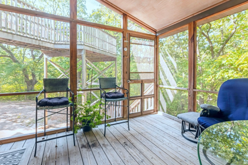 A screened porch with two chairs, a small table, and a view of trees outside. Natural light fills the space.