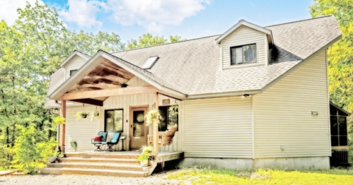 A spacious, modern house with a front porch surrounded by trees under a bright blue sky.
