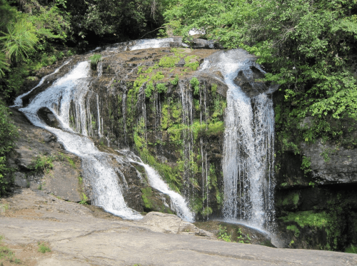 A serene waterfall cascading over rocks, surrounded by lush greenery and moss.