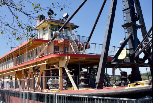 A close-up of a riverboat with a red and yellow exterior, featuring a pilot house and machinery on deck.