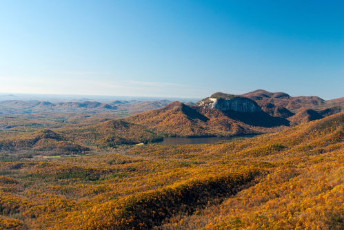 A panoramic view of autumn-colored mountains and a lake under a clear blue sky.