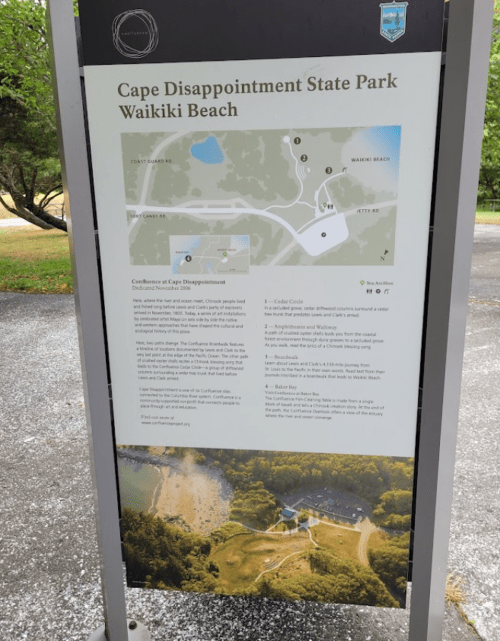 Sign at Cape Disappointment State Park detailing park information and map, with a view of Waikiki Beach below.