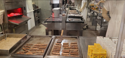 A bakery kitchen with trays of baked goods, a large oven, and various utensils on stainless steel counters.