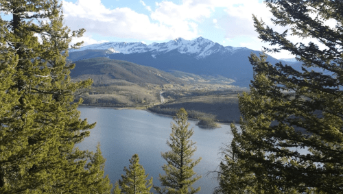 A scenic view of a lake surrounded by mountains and pine trees under a partly cloudy sky.