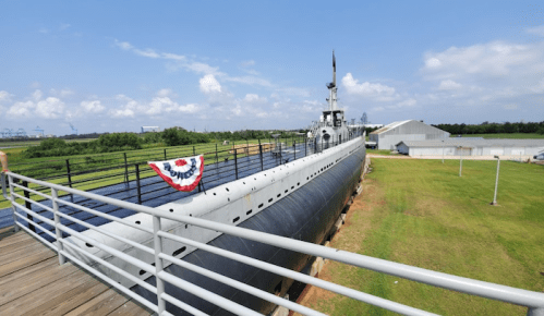 A submarine on display at a museum, surrounded by green grass and blue skies, with a walkway leading to it.