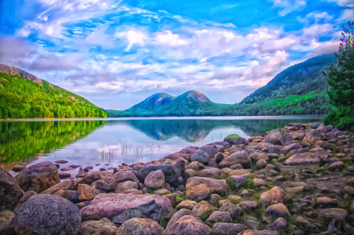 A serene lake surrounded by mountains, with a rocky shore and a reflection of clouds in the water.
