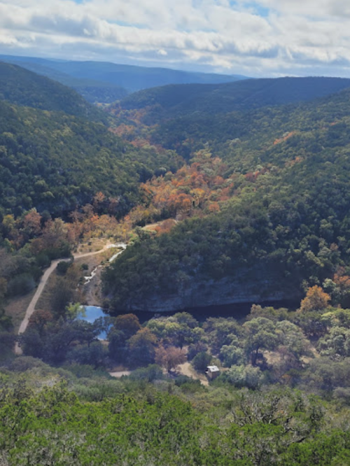 A scenic view of a lush valley with colorful autumn foliage, a winding river, and a small cabin nestled among the trees.