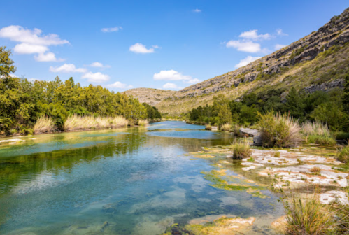 A serene river flows through a lush landscape, surrounded by hills and clear blue skies.