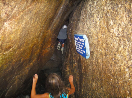 A child climbs through a narrow cave passage, with a sign nearby indicating the location.