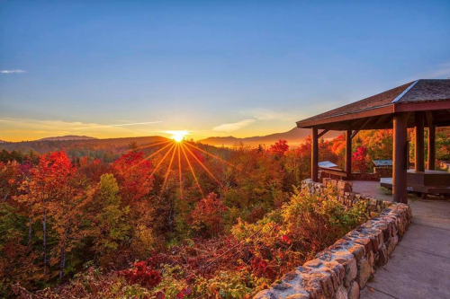 A vibrant sunset over a colorful autumn landscape, viewed from a gazebo with stone walls.
