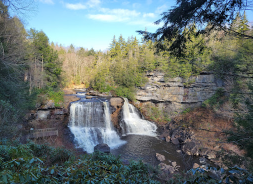 A scenic waterfall surrounded by lush greenery and rocky cliffs under a clear blue sky.