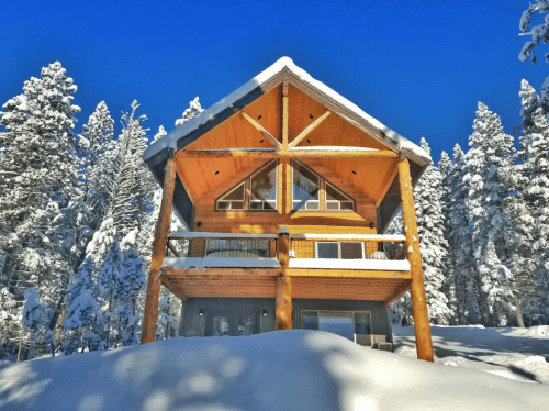 A cozy wooden cabin surrounded by snow-covered trees under a clear blue sky.