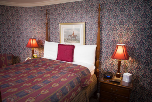 Cozy bedroom with a patterned wallpaper, a four-poster bed, and bedside lamps, featuring a framed horse painting.