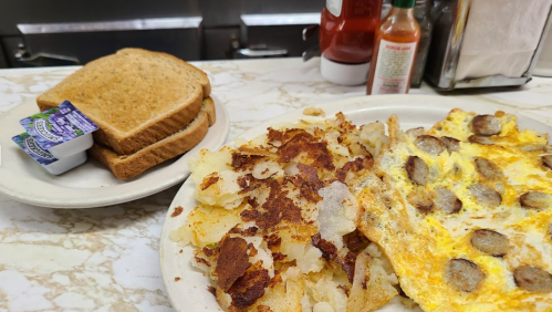 A plate of scrambled eggs with sausage and crispy hash browns, alongside a plate of toast and condiments.