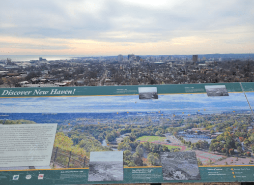 A panoramic view of New Haven with a scenic overlook sign in the foreground, showcasing the city and coastline.