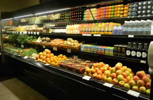 A well-stocked grocery display featuring various fruits, vegetables, and beverages on shelves.