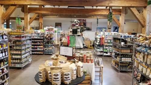 A spacious grocery store with wooden beams, featuring shelves of various food products and a central display of snacks.