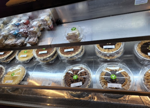 Display case filled with various pies and desserts, including cheesecakes and layered cakes, all labeled.