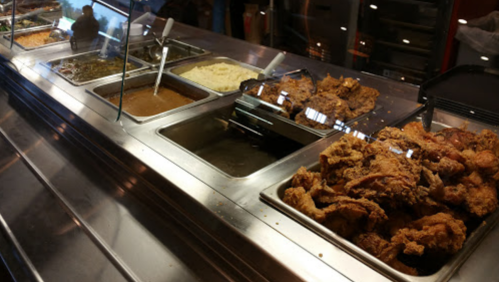 A buffet display featuring fried chicken, mashed potatoes, gravy, and various side dishes in metal trays.