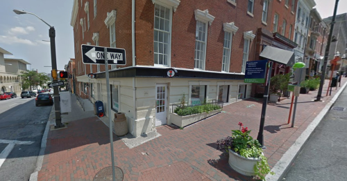 Street view of a brick building on a corner, featuring a sign for a one-way street and planters along the sidewalk.