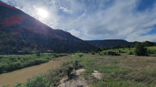 A scenic view of a river winding through green hills under a bright sky with scattered clouds.