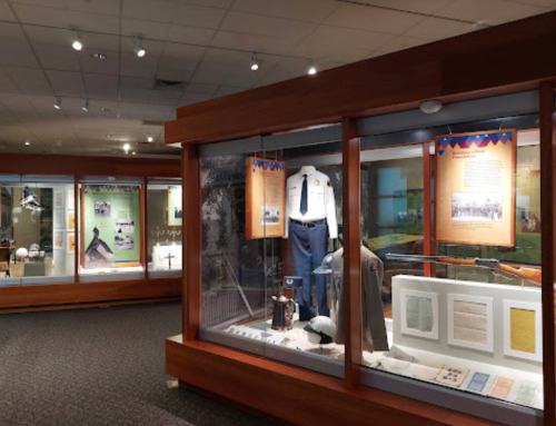 Exhibit display in a museum featuring uniforms, artifacts, and informational panels in glass cases.