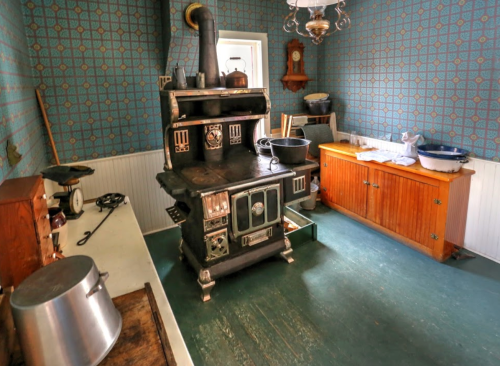 A vintage kitchen featuring an old stove, wooden cabinets, and patterned wallpaper.