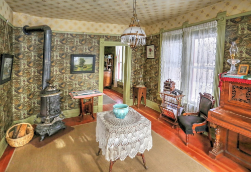 A vintage room with patterned wallpaper, a decorative table, a wood stove, and antique furniture.