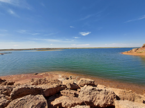 A serene lake surrounded by rocky shores under a clear blue sky with a few clouds.
