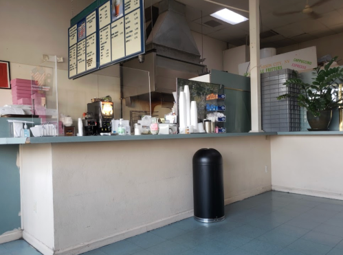 A cafe interior with a counter, menu board, coffee machine, and a black trash can in a clean, simple space.