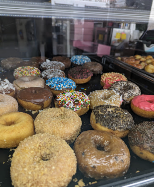 A variety of colorful donuts displayed in a case, featuring sprinkles, chocolate, and different toppings.