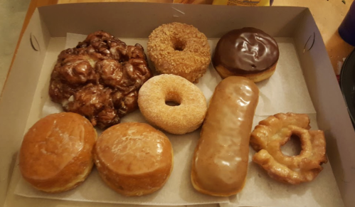 A box of assorted donuts, including glazed, chocolate-covered, and a cruller, arranged on parchment paper.