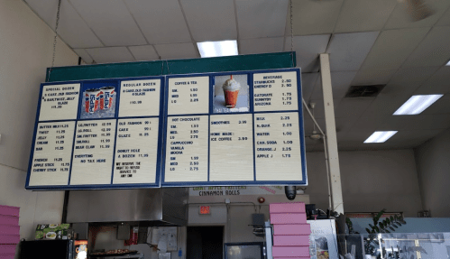 Menu board displaying various food and drink items with prices, including donuts, coffee, and beverages.