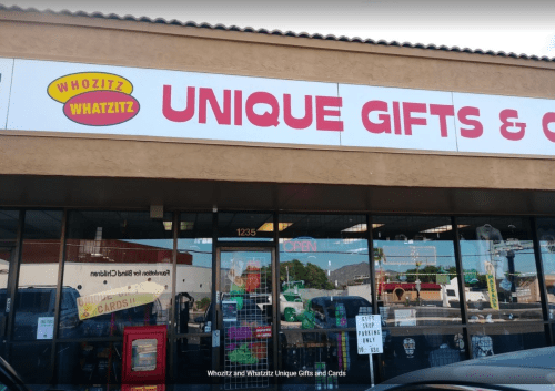 Storefront of "Whozitz and Whatzitz Unique Gifts & Cards," featuring a colorful sign and open entrance.