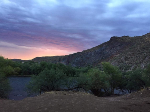 A serene landscape featuring a river surrounded by hills and trees under a colorful twilight sky.