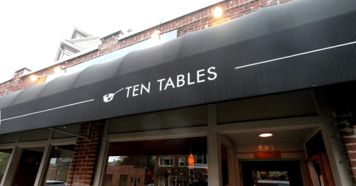 Exterior of a restaurant called "Ten Tables," featuring a black awning with white lettering and a brick facade.