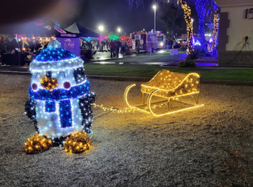 A lit penguin decoration pulling a glowing sleigh, set in a festive outdoor scene with colorful lights.