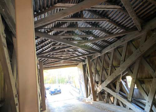Interior view of a covered bridge, showcasing wooden beams and a glimpse of a car passing through.