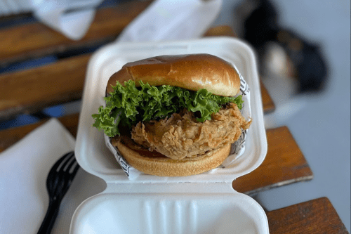 A crispy fried chicken sandwich with lettuce on a soft bun, served in a takeout container.