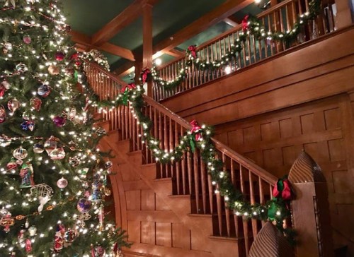 A beautifully decorated staircase with garlands and a Christmas tree adorned with ornaments and lights.