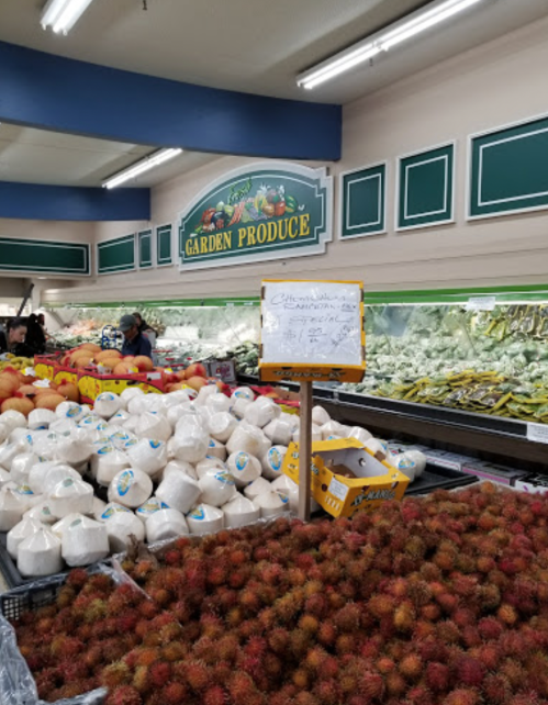 A produce section featuring various fruits, including rambutan and coconuts, with a sign for Garden Produce.