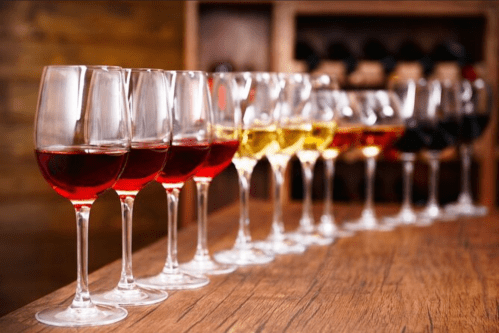 A row of wine glasses filled with various types of red, white, and yellow wines on a wooden table.