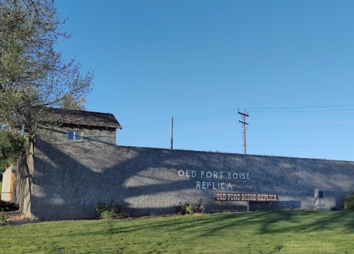 A replica of Old Fort Boise with a sign, set against a clear blue sky and green grass.
