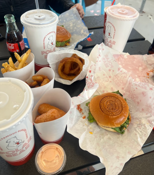 A table with fast food including burgers, fries, onion rings, chicken bites, and drinks from Polar Bear.