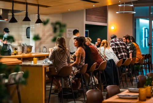 A lively restaurant scene with people seated at a bar, enjoying food and drinks in a warm, inviting atmosphere.