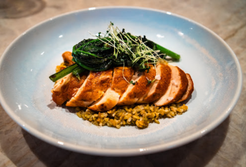 Grilled chicken breast sliced on a bed of bulgur wheat, topped with sautéed greens and microgreens.