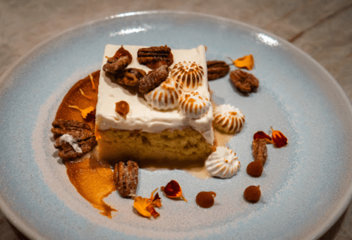 A slice of cake topped with cream, decorative meringues, pecans, and edible flowers on a blue plate.