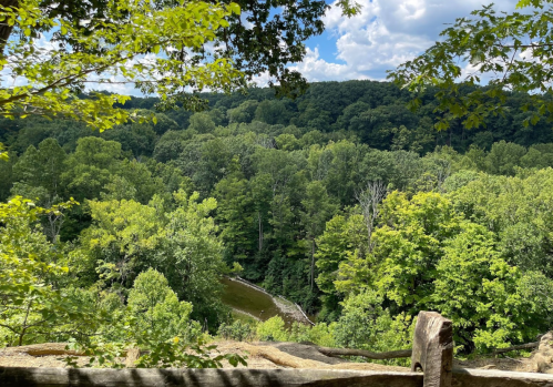 Lush green trees and a winding river are visible in a scenic landscape under a partly cloudy sky.